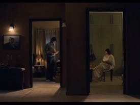A still from Hindi film, ‘Do Aur Do Pyaar (2024)’. A wide-ish frame that shows through two doors into dark-ish rooms of a house. One room has a man looking into his phone and the other has a woman looking into hers.