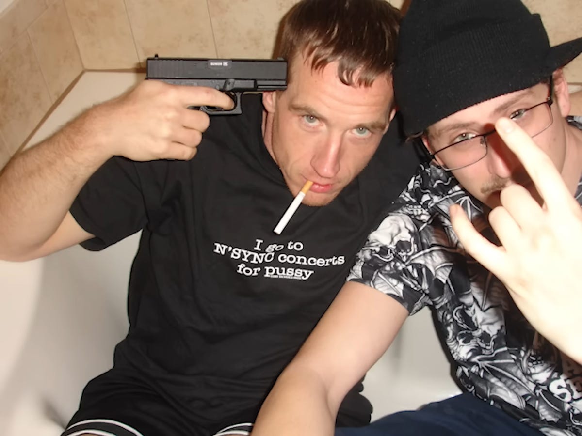 A photo of Connor O'Malley sitting in a bathtub, posing by pointing a gun at his head and wearing a t-shirt that says "I go to N'SYNC concerts for pussy". Danny Scharar is sitting to his left, partially outside the frame, pulling a gang sign.