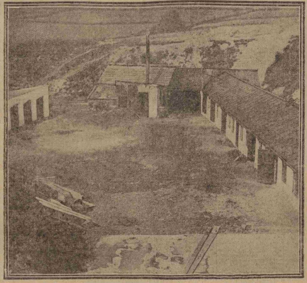 A photograph of a farmyard, with long low buildings on three sides. Beyond is moorland scenery.