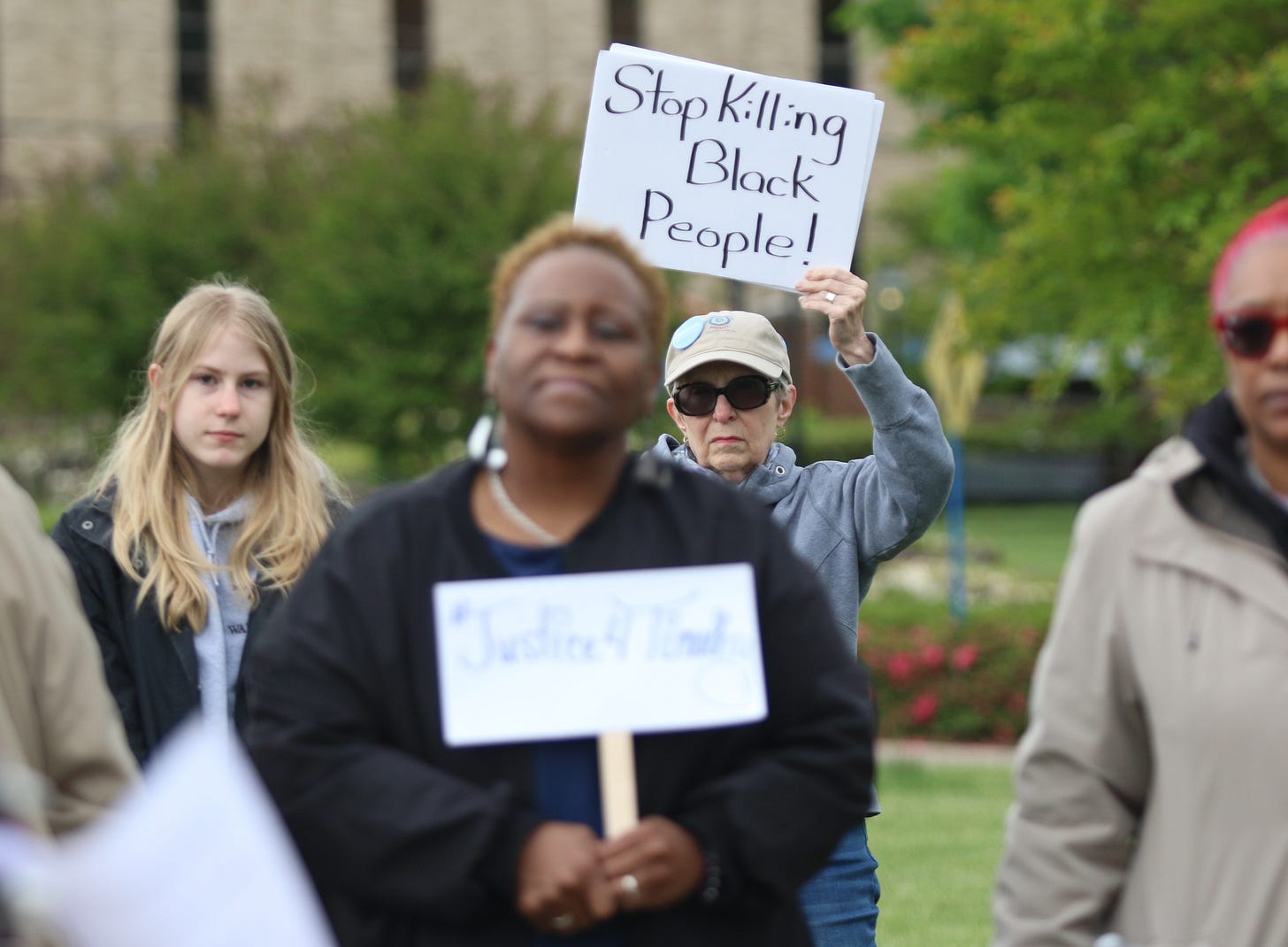 A woman standing behind Melissa Johnson holds a sign at a May 2nd rally in support of the family of Timothy Johnson in Fairfax.