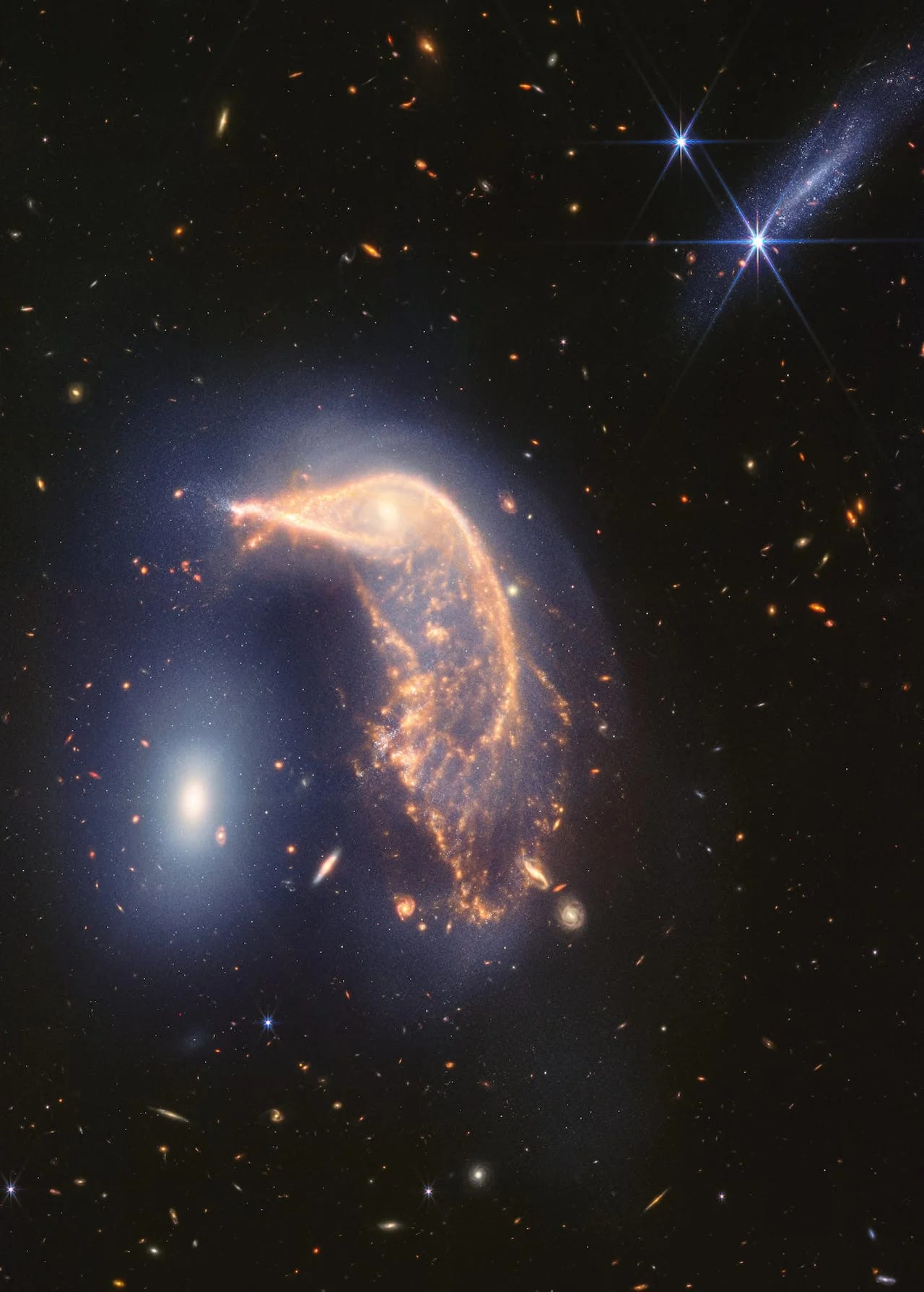 A large yellow-white galaxy stands out against the blackness of deep space. The galaxy is shaped like a penguin, with a smaller, bright white galaxy to its left that is shaped like an egg. 