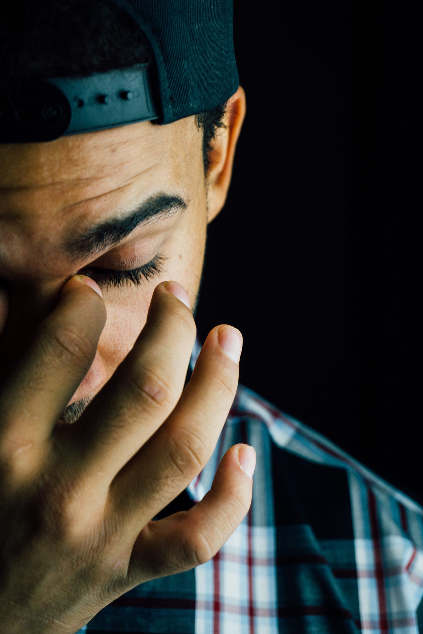 Close up portrait of a man wearing a backwards baseball cap. He looks tired, pinching the bridge of his nose.