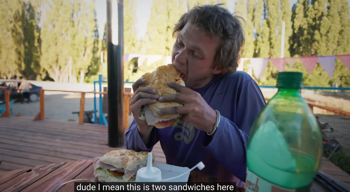 Un mec prenant une grande bouchée d'un énorme sandwich