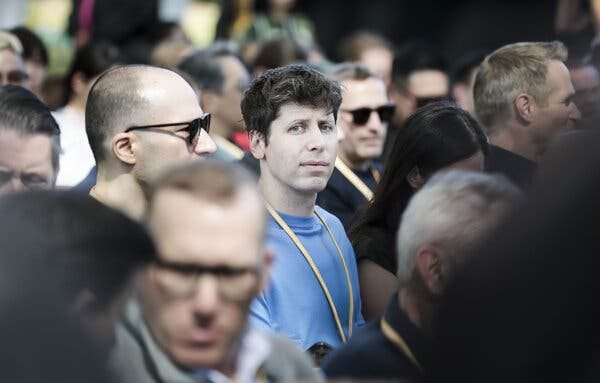 Sam Altman, in a blue shirt, stands in a crowd.