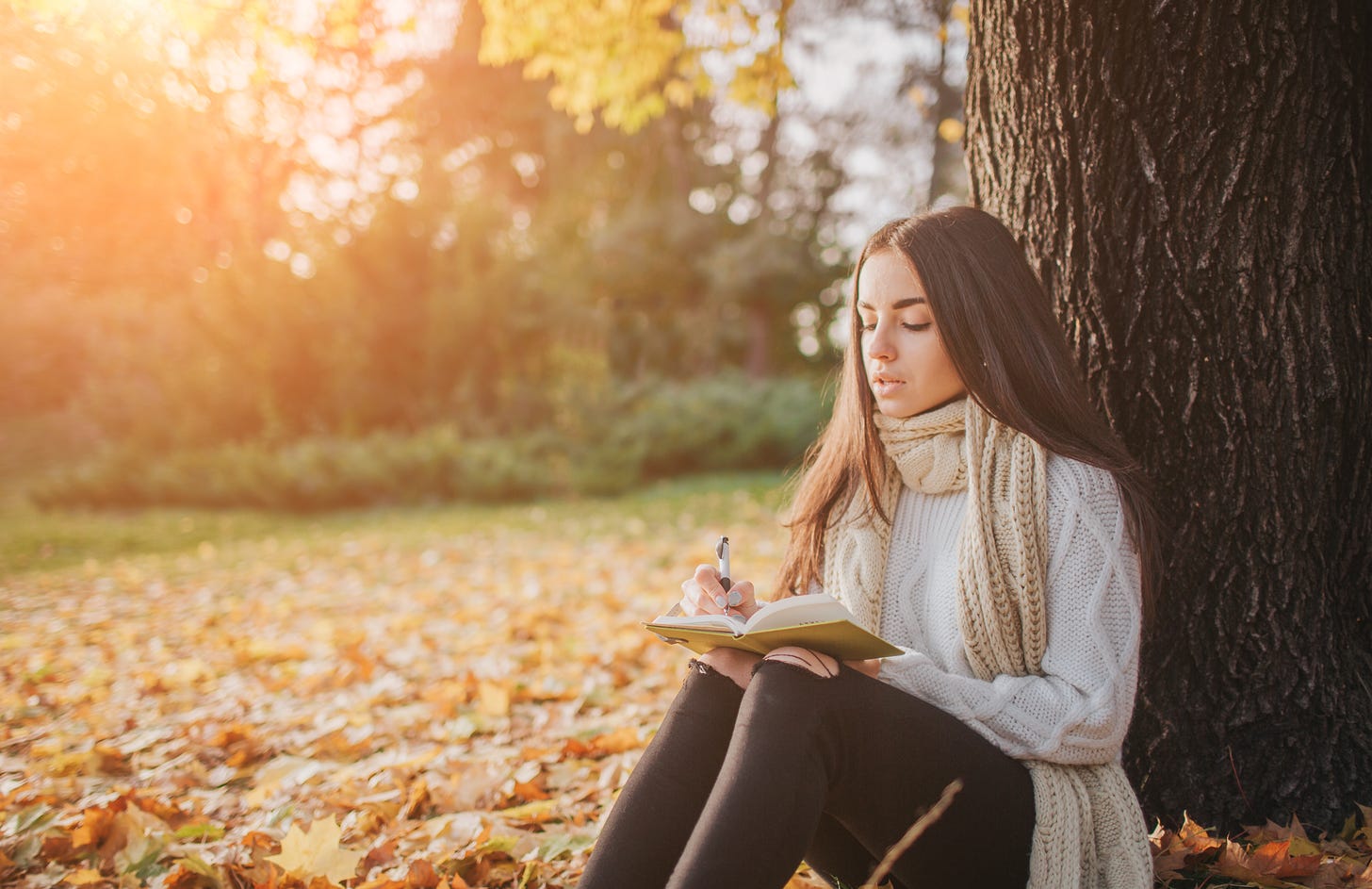 Girl sitting next to a tree writing in a journal