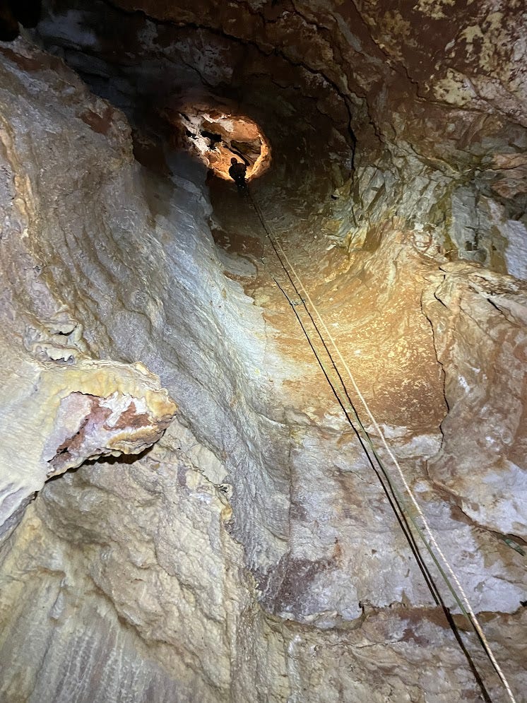 A caver lead climbing high up in a tall pit