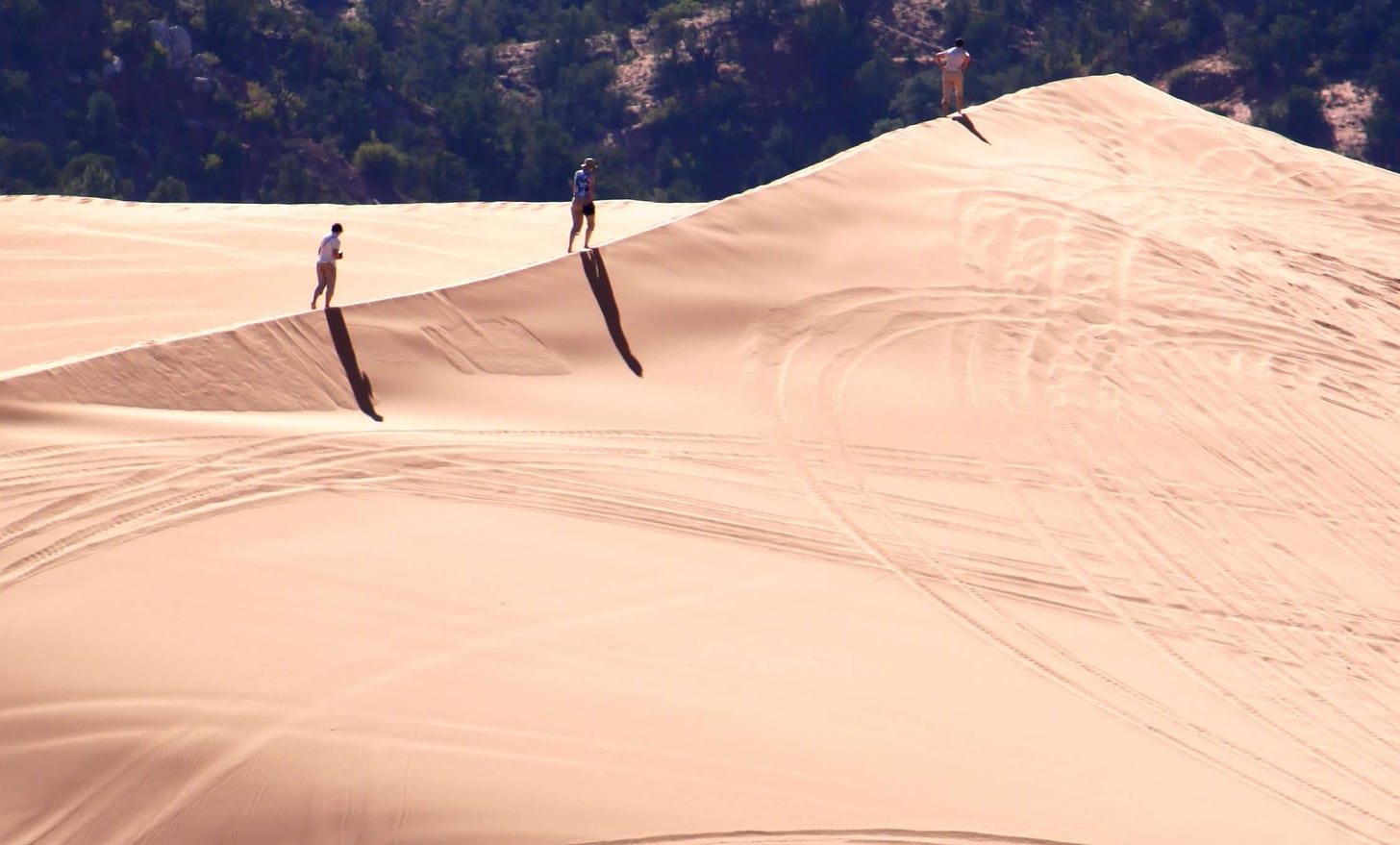 three hikers on a pink sand dune