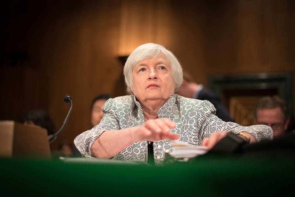 An old white woman with white hair, sitting with a microphone