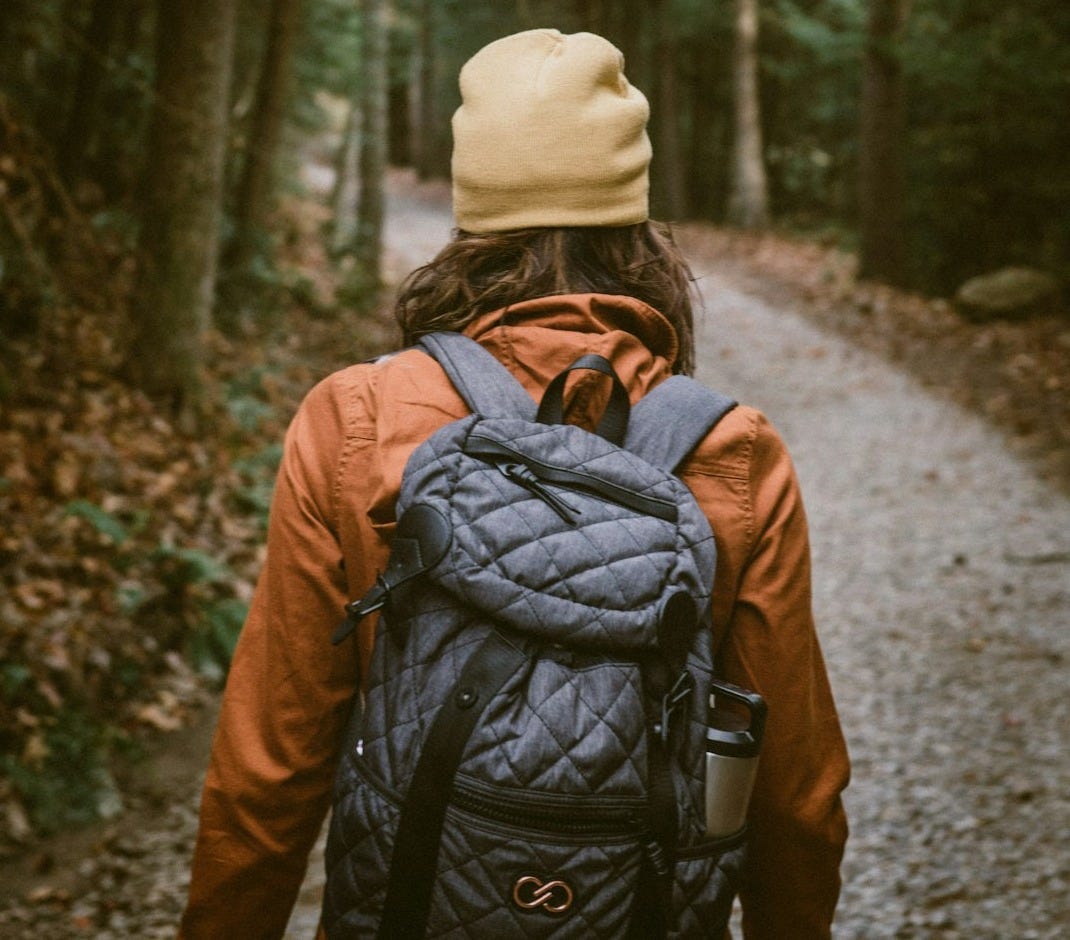 woman carrying backpack walking towards the forest