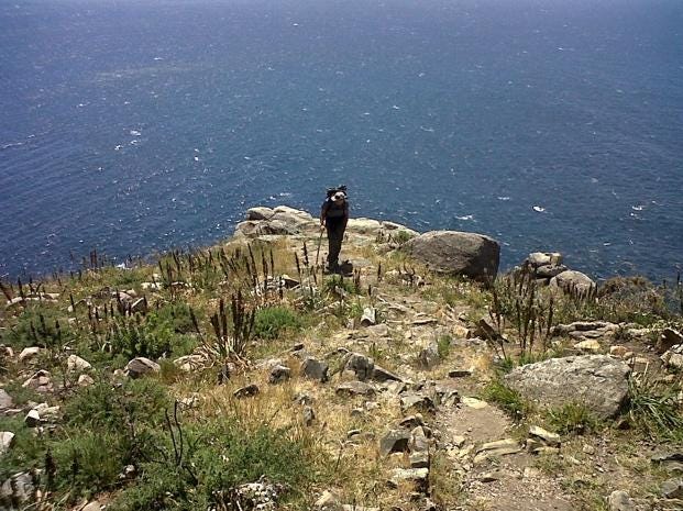 A person standing on a rocky hill overlooking the ocean

Description automatically generated