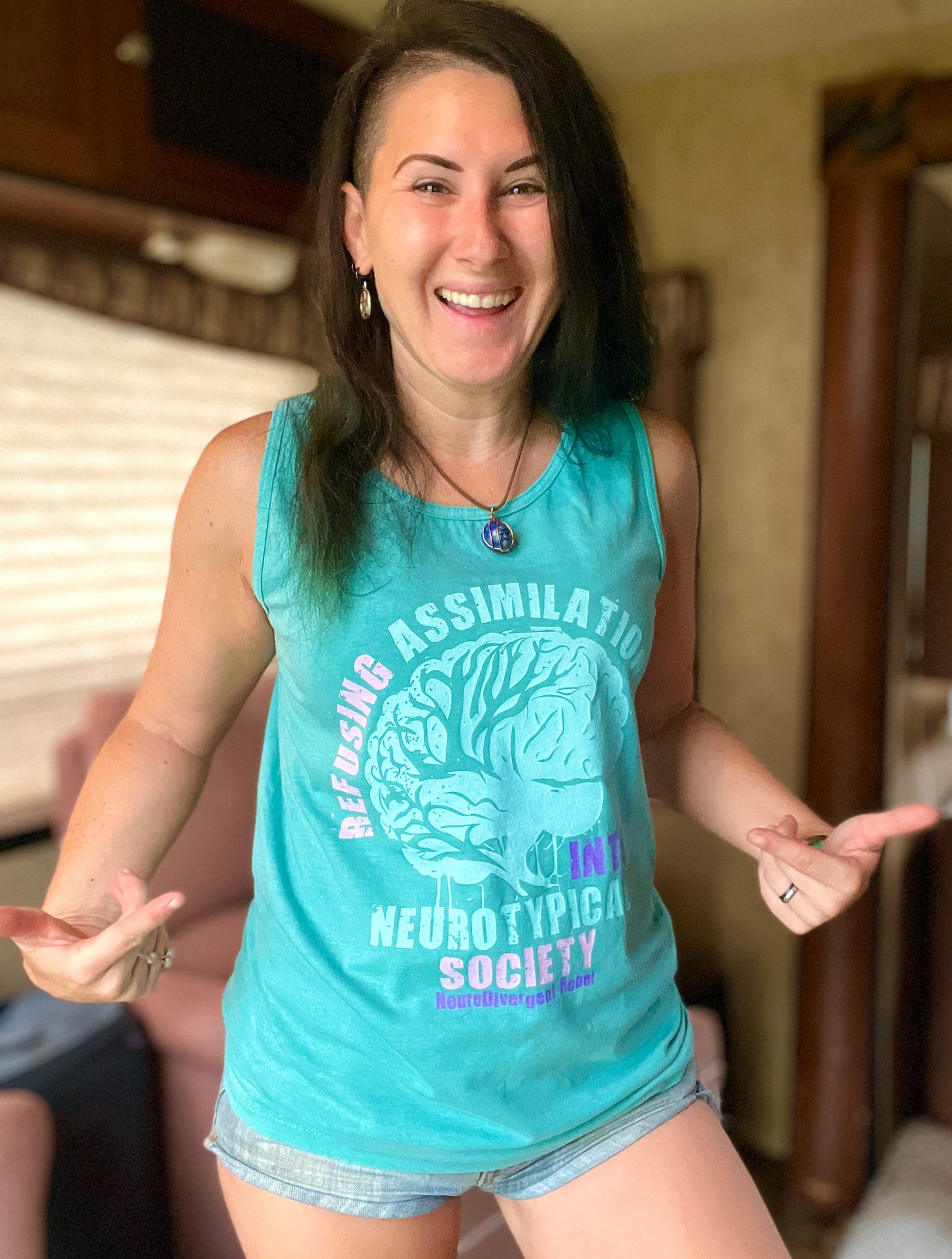 Lyric Rivera, in a teal shirt that reads “Refusing Assimilation Into NeuroTypical Society”