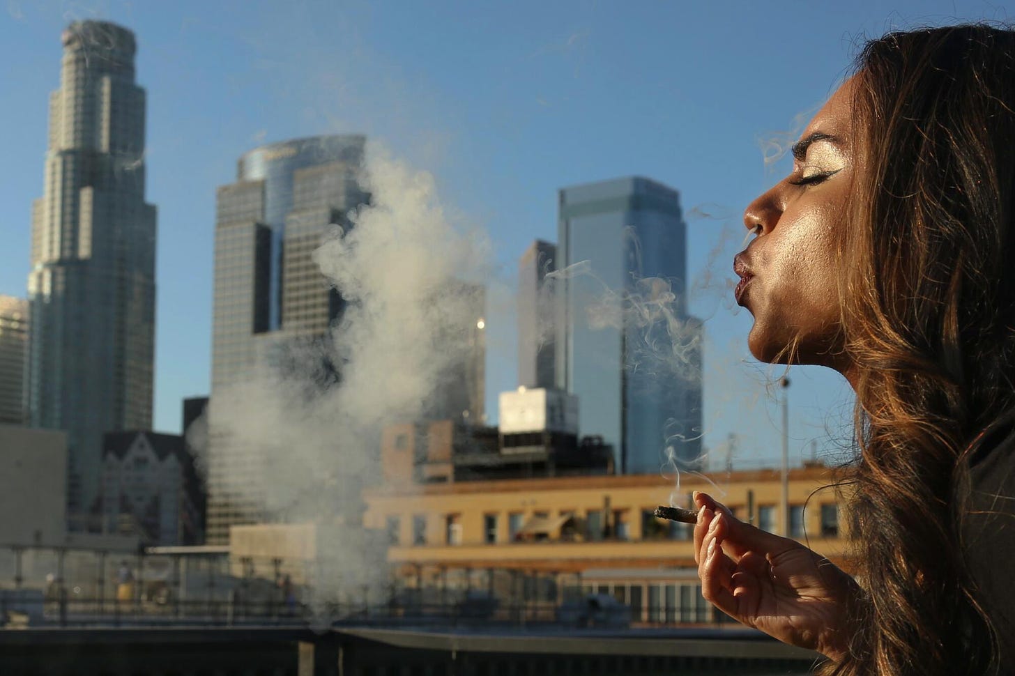 A woman exhales smoke over the downtown L.A. skyline.
