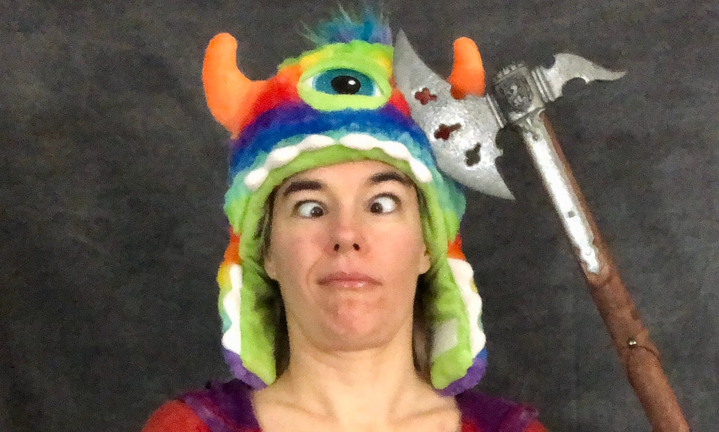 The author, cross-eyed in a rainbow monster hat with an axe alongside her head