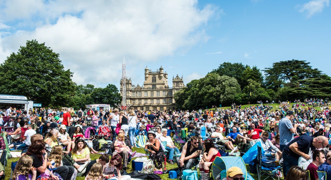A crowd of people sitting on a lawn outside Wollaton Hall