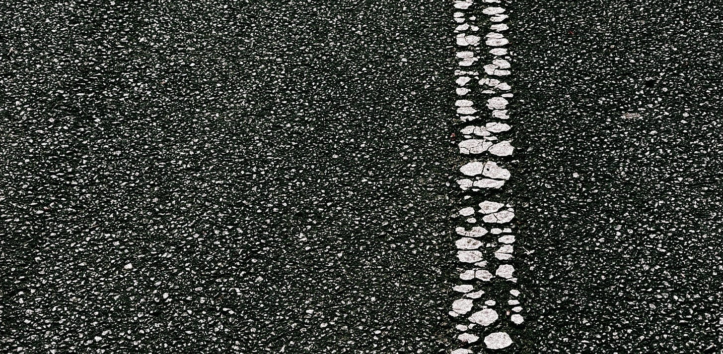 Cracked white line running from top to bottom of image with close of asphalt