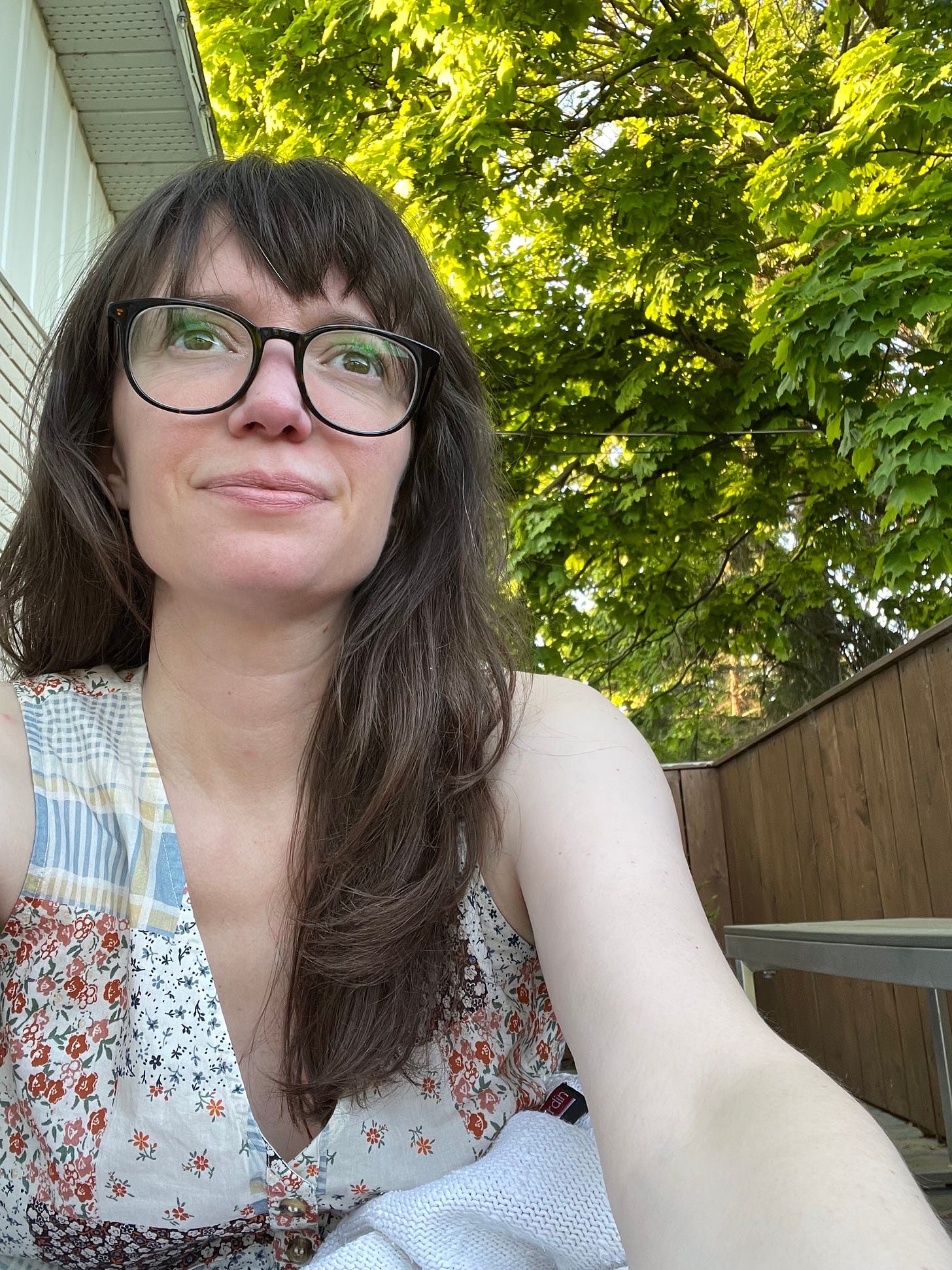 a white woman with long brown hair takes a selfie under a maple tree