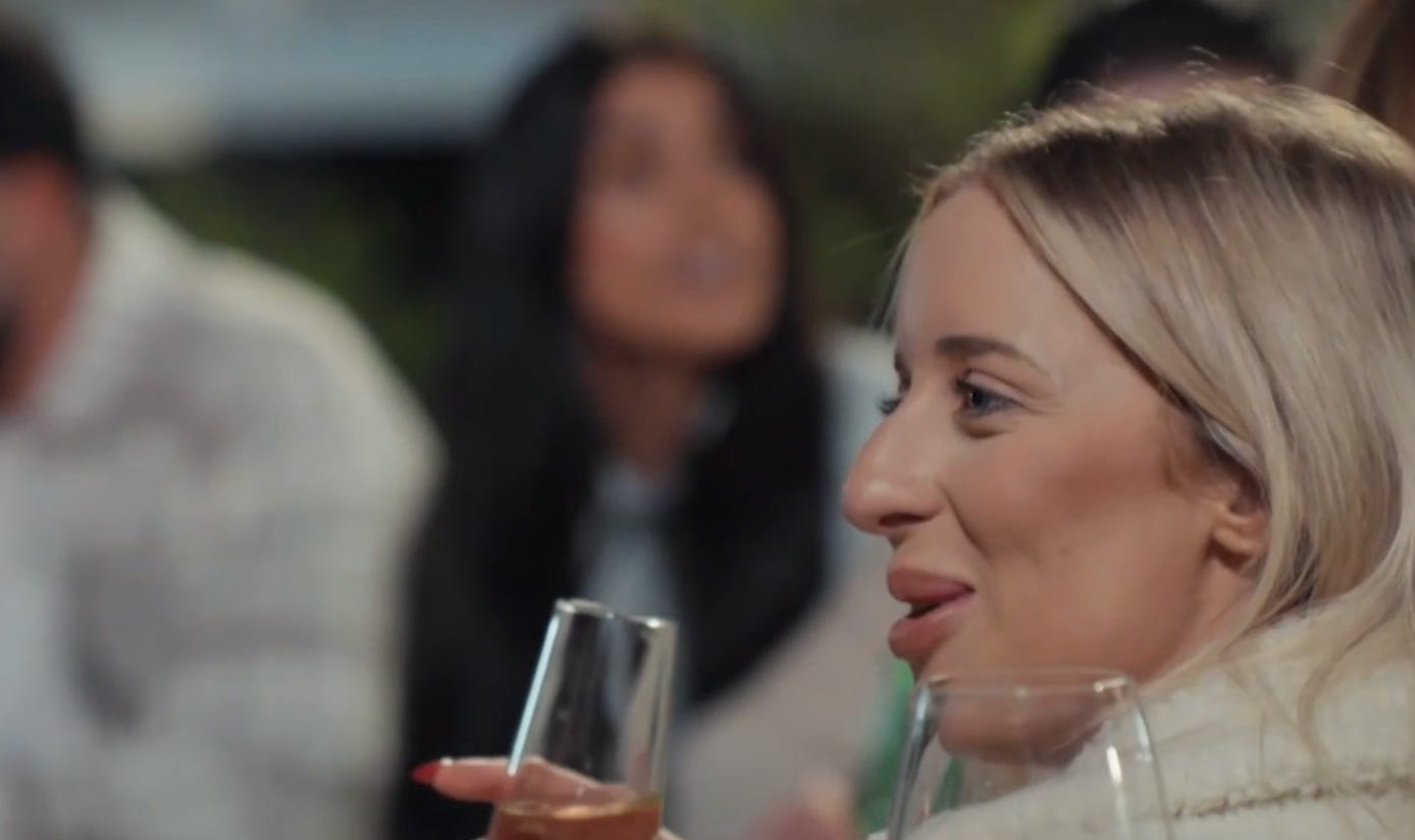 Jamie from MAFS 2025 smirks while holding a champagne glass at a social gathering