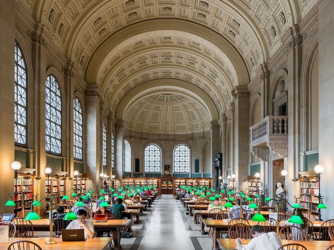 Picture of the boston public library with many people studying at tables in it's interior