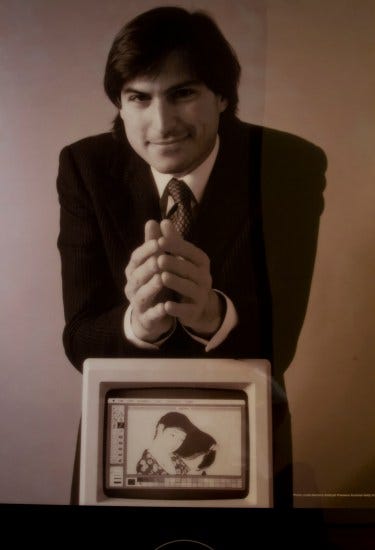 Young Steve Jobs in a suit and tie leans forward with hands folded, on a small Apple monitor which displays a digital rendering of the Goyo print in MacPaint. 