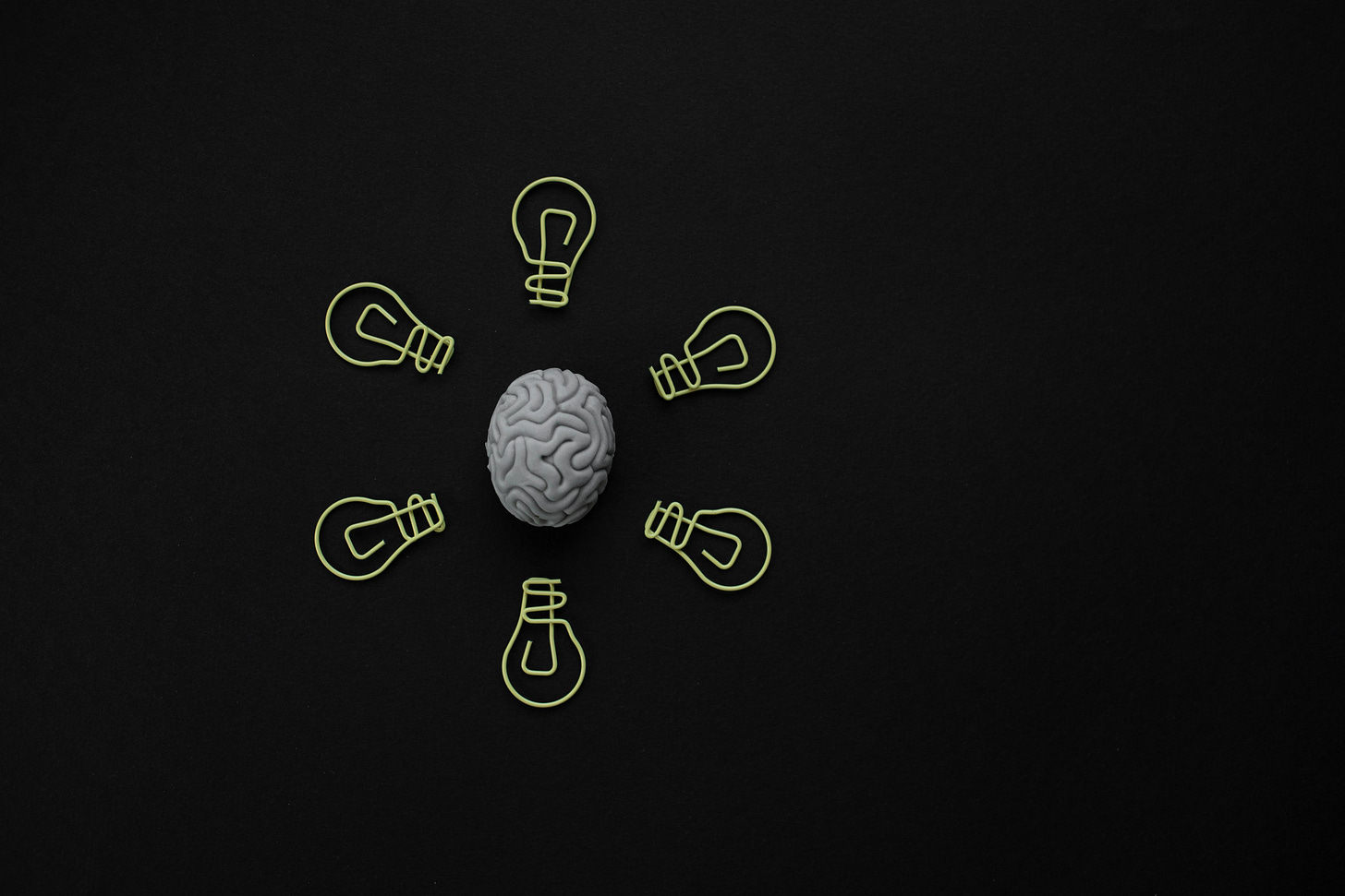 A grey brain on a black background surouned by yellow paper clips.