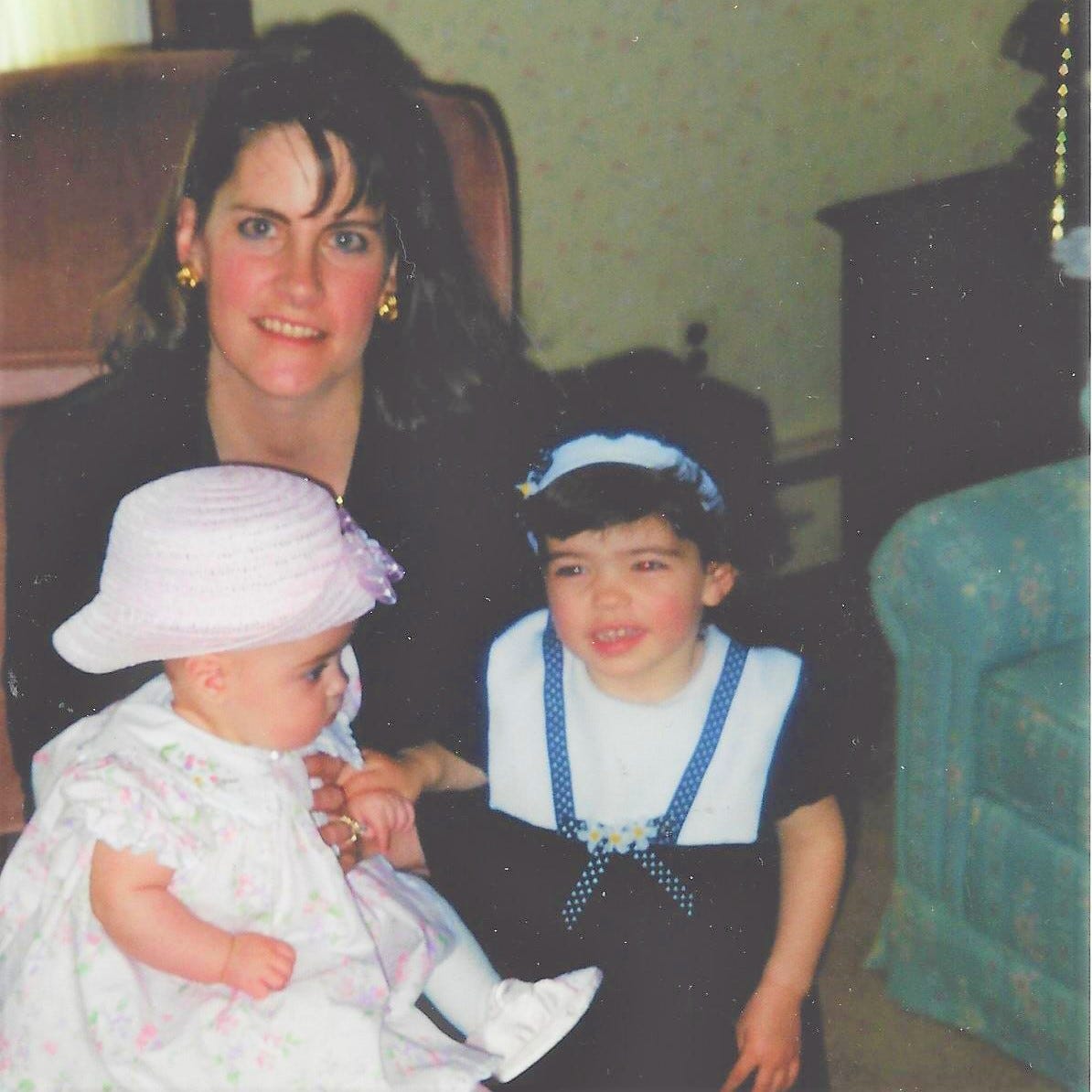 A young slightly bedraggled mother posed with a baby and a toddler in their Easter finest