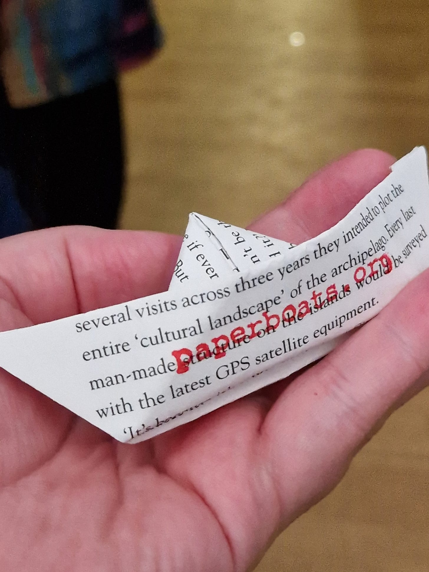 An origami paper boat made from a page of one of Kathleen Jamie's essays. Features the web address paperboats.org