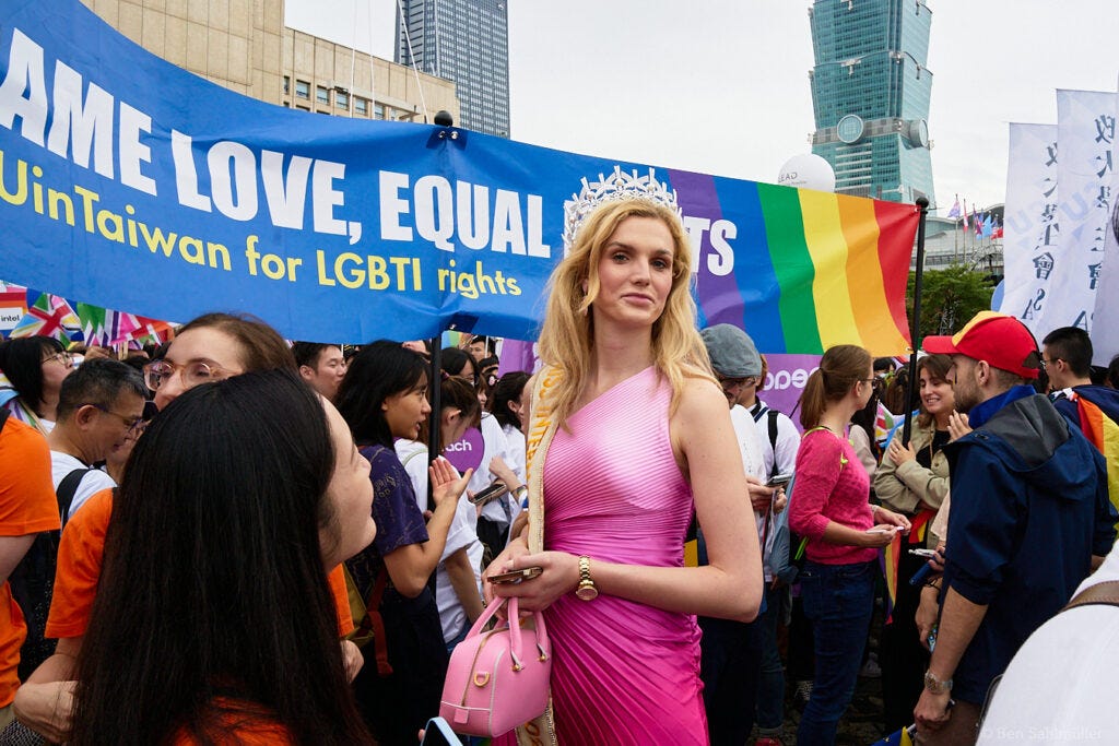 A tall blond woman dressed in a shiny pink dress stands in front of the EU group's banner. The banner reads "Same Love, Equal Rights."