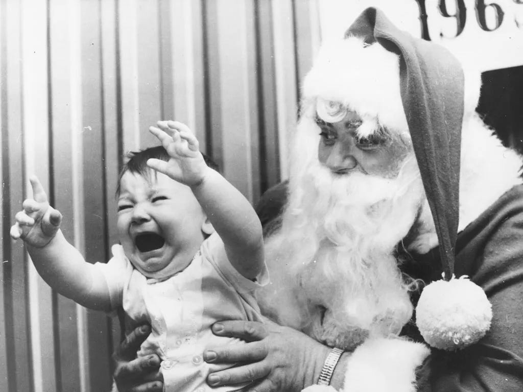 Black and white photo of child on Santa's lap crying with upraised arms trying to leave. Keystone/Getty Images