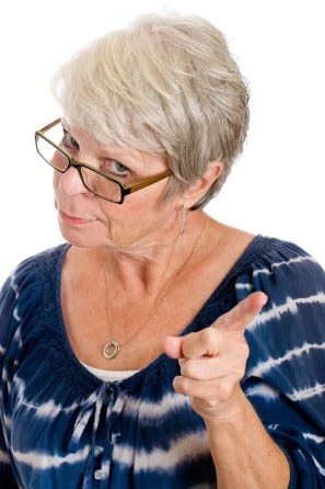 Middle aged stern-faced woman looking over her glasses and wagging her finger disapprovingly.