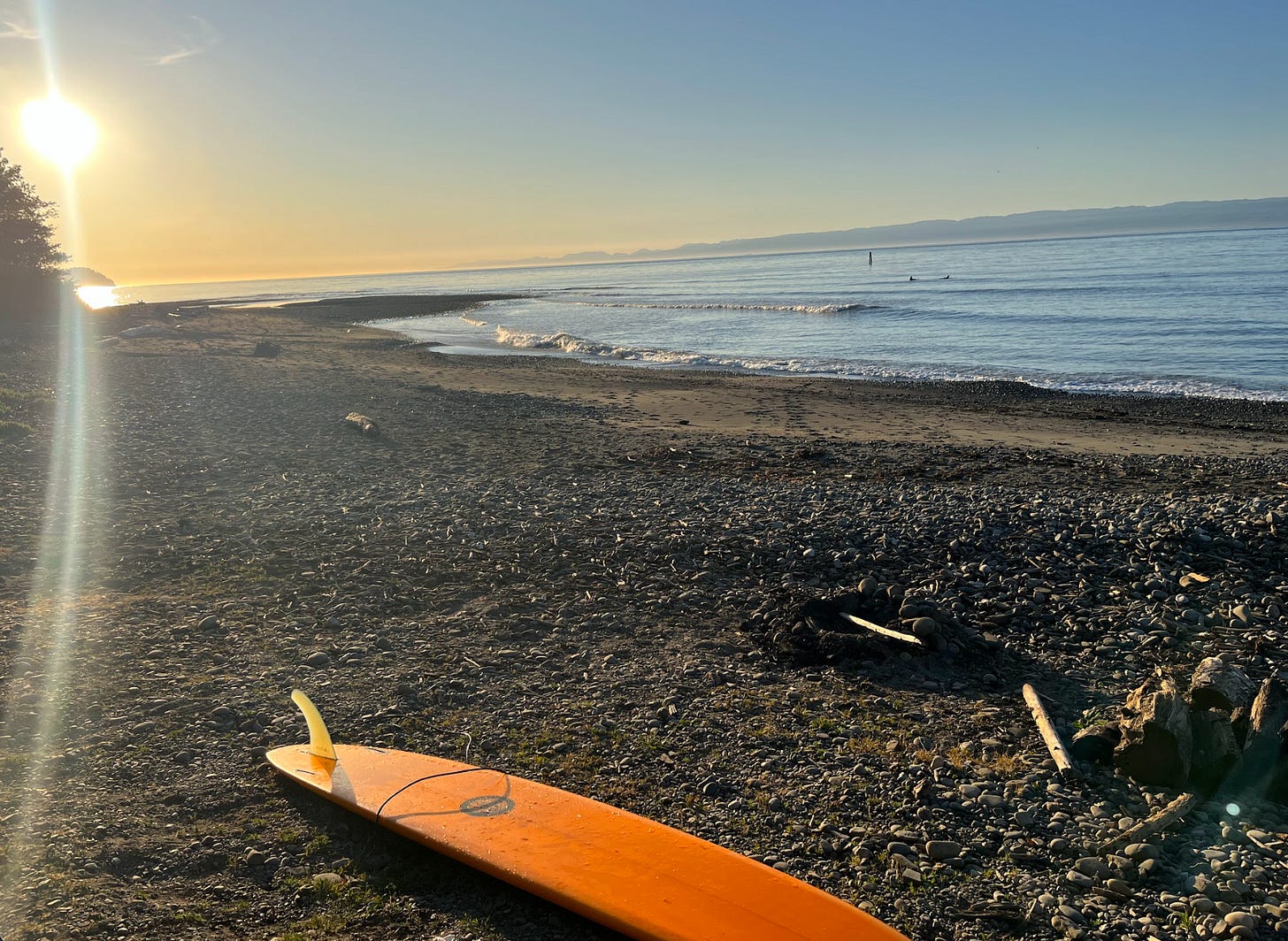 orange surfboard on rocky beach at sunset