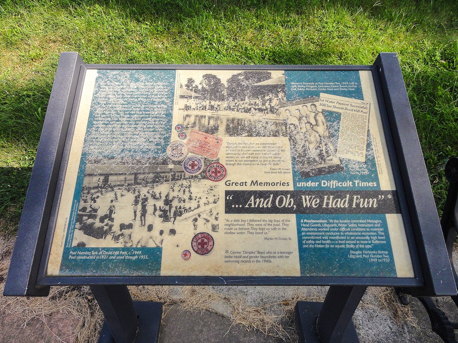 This photograph shows an interpretive sign for the Druid Hill Pool No. 2 memorial. The sign is weathered and not very readable. However, its largest text is clear and reads: “Great Memories Under Difficult Times” and “…And Oh, We Had Fun.”