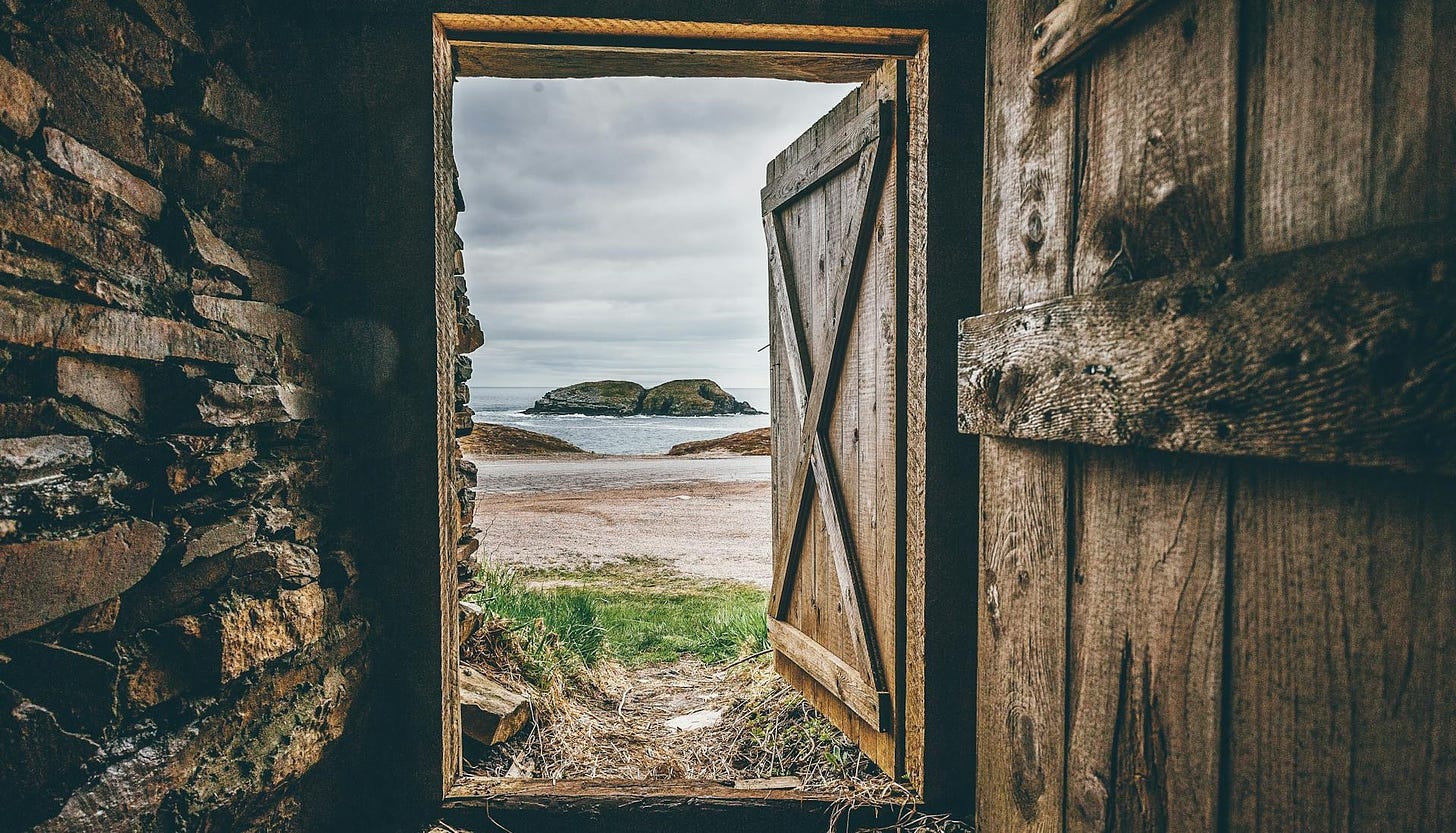 A rough-hewn door, standing open. Beyond it, a beautiful oceanscape and beach.