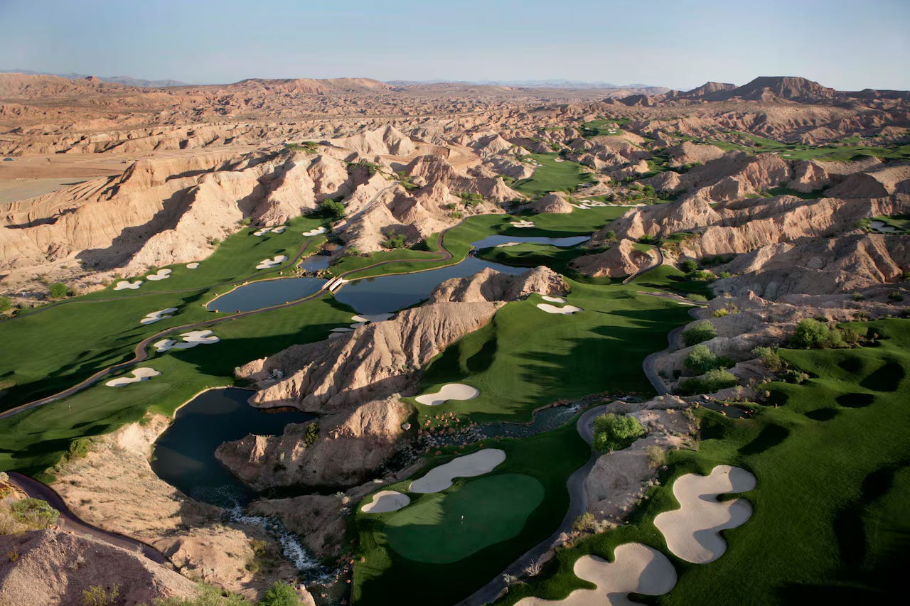 Aerial photograph of Wolf Creek Golf Club showing emerald green fairways and white sand bunkers dramatically woven through desert canyon landscape. Multiple water features reflect the blue sky amid the rocky terrain. Aerial photograph of Wolf Creek Golf Club showing emerald green fairways and white sand bunkers dramatically woven through desert canyon landscape. Multiple water features reflect the blue sky amid the rocky terrain.
