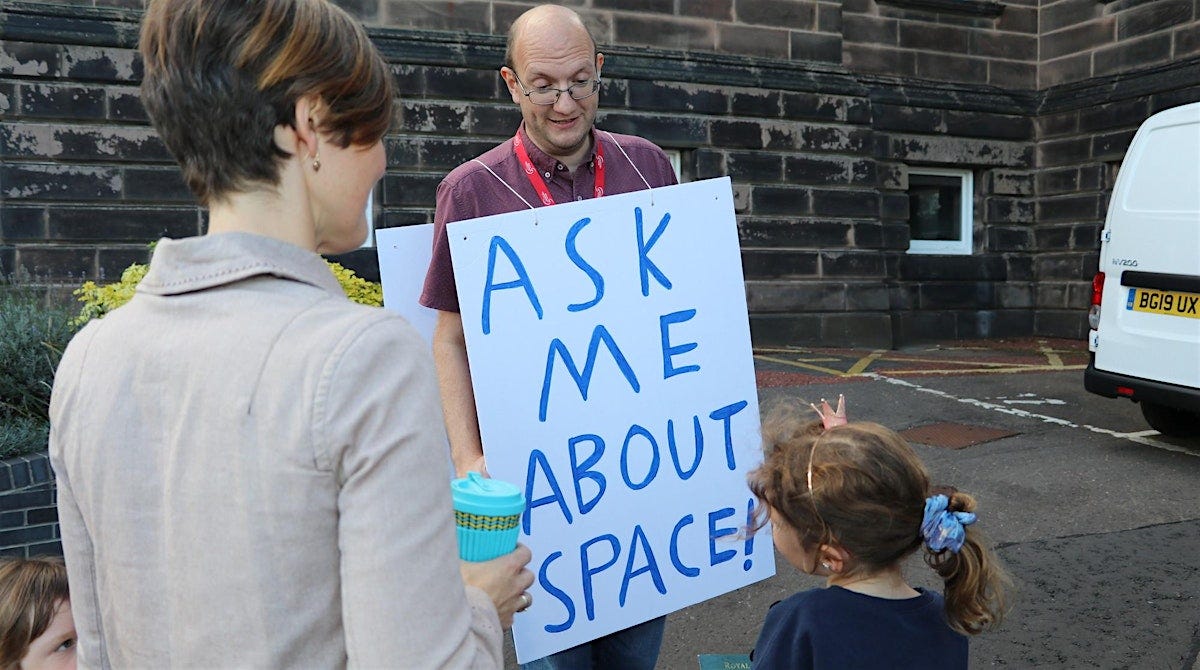 Woman and child facing a man wearing a sandwich board which reads: "ask me about space"