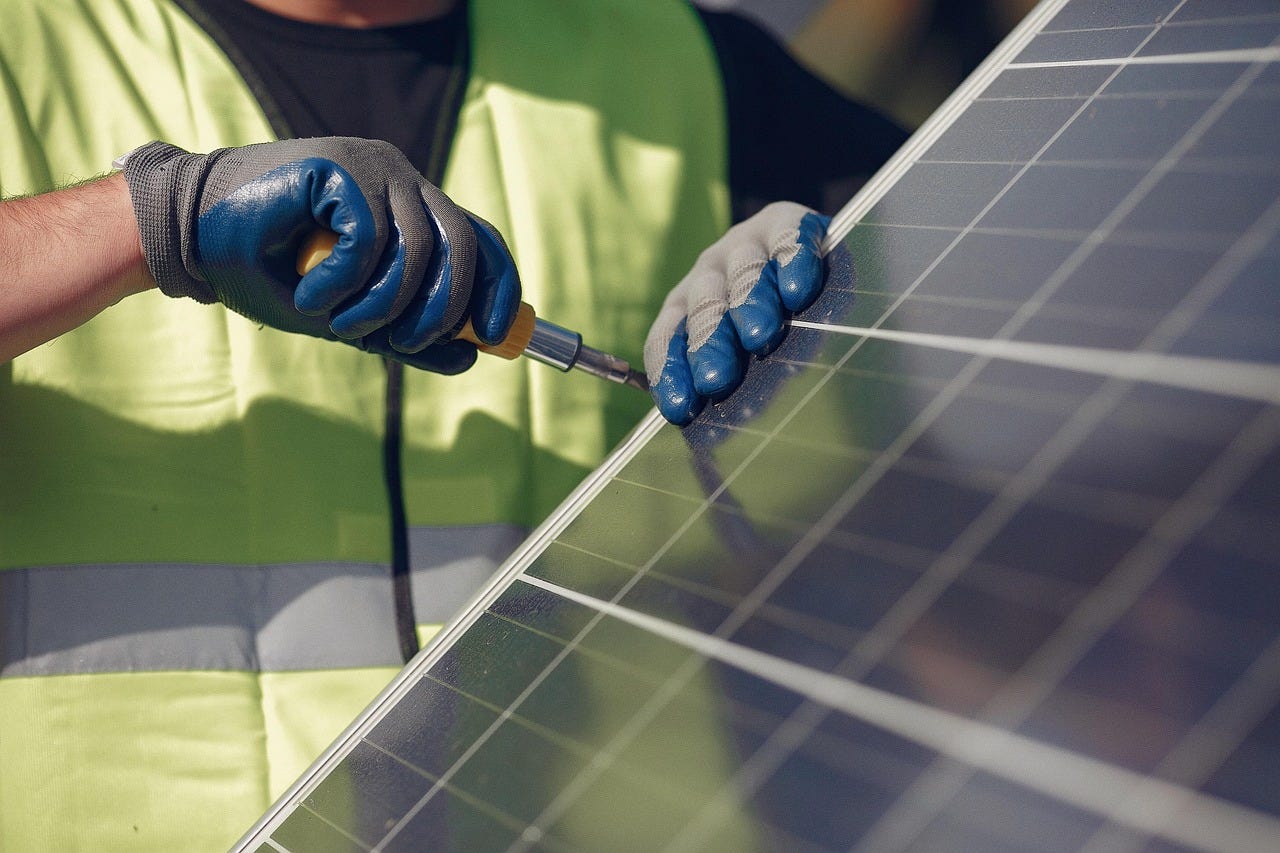 A worker is using what looks like a screw driver on the end of a solar panel, apparently doing some work to install it A worker is using what looks like a screw driver on the end of a solar panel, apparently doing some work to install it