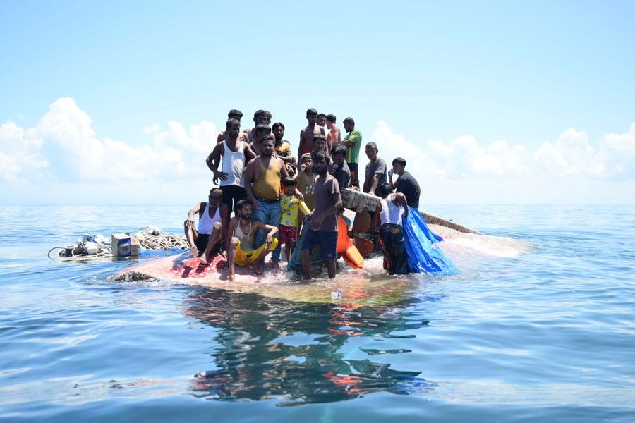 A group of people cluster together on the hull of an overturned boat at sea.