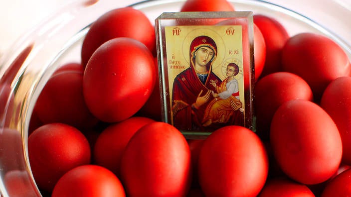 A bowl of eggs dyed red with a small icon of Mary and Jesus sitting in the center.
