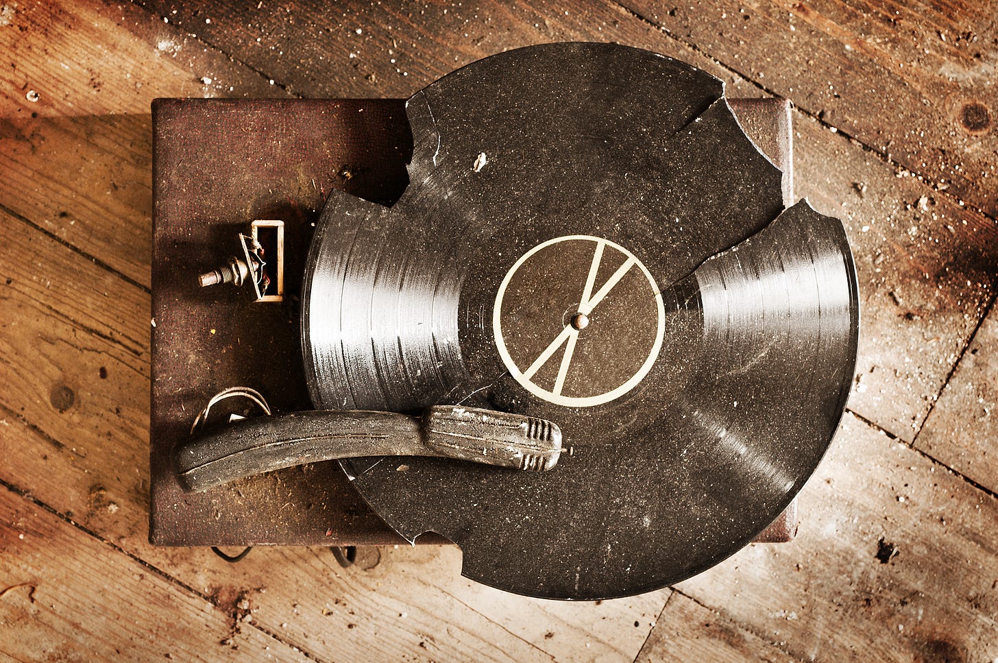 The image of a wooden record player on a wood-slatted floor, playing a dusty, broken record.