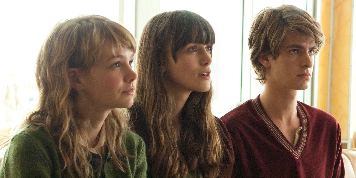 Photo of Carey Mulligan (as Kathy), Keira Knightley (as Ruth), and Andrew Garfield (as Tommy) sitting in a row and all looking up at someone, from the movie Never Let Me Go