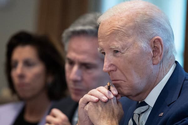 President Biden clasps his hands beneath his chin, holding a pen.