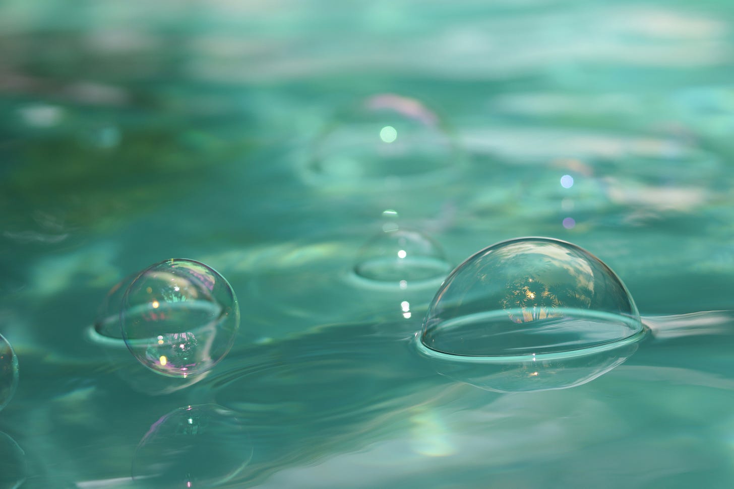 Bubbles sitting on bright aquamarine water. They reflect light and you can make out palm trees in the reflection of one of them.