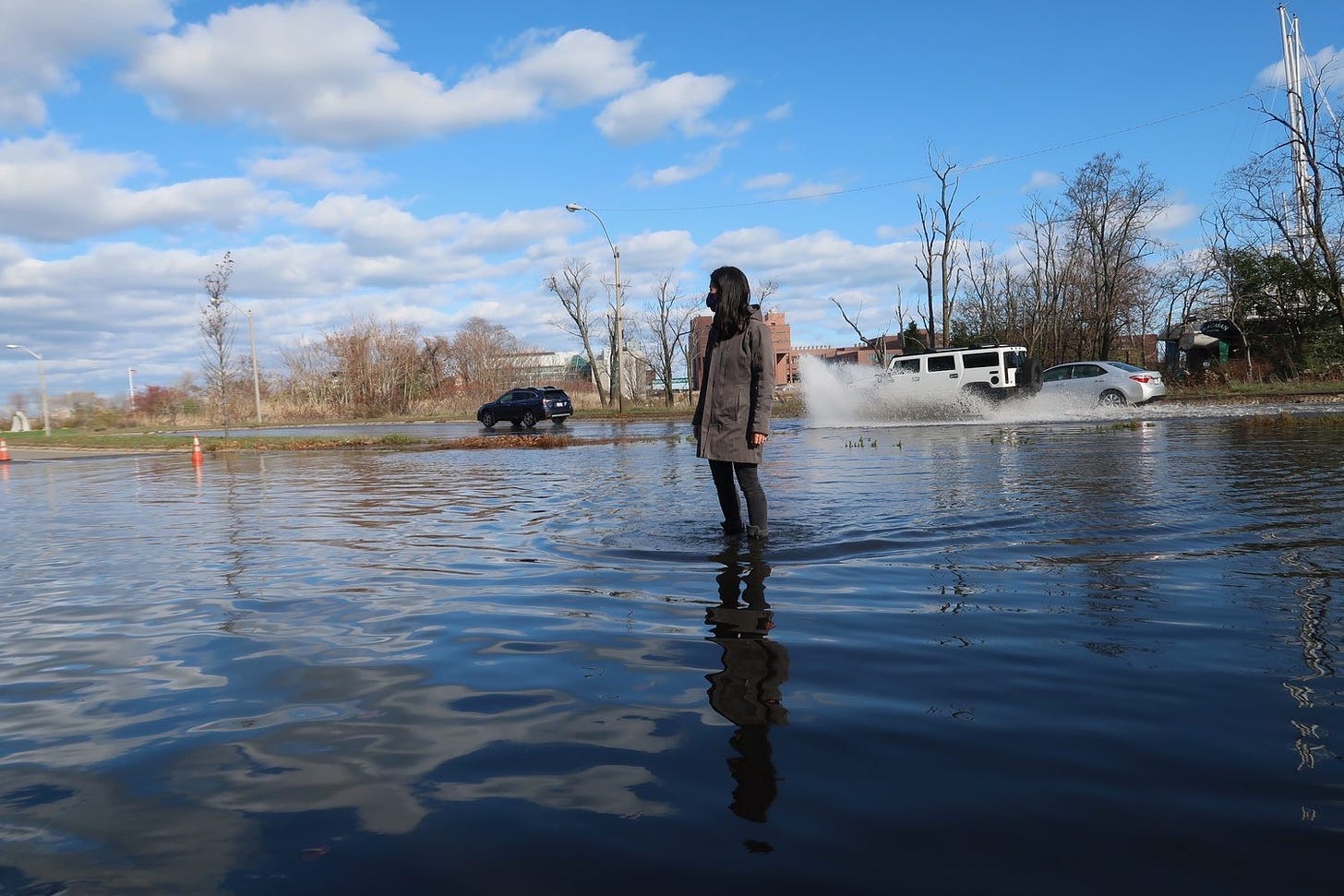 Michelle stands in ankle deep water looking both ways to cross a completely flooded Morrissey Blvd under blue skies