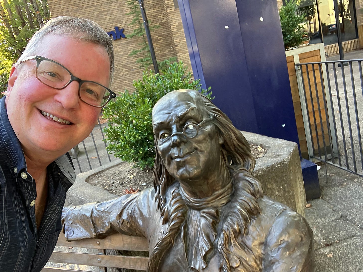 Ben Franklin sitting on a bench with man wearing glasses