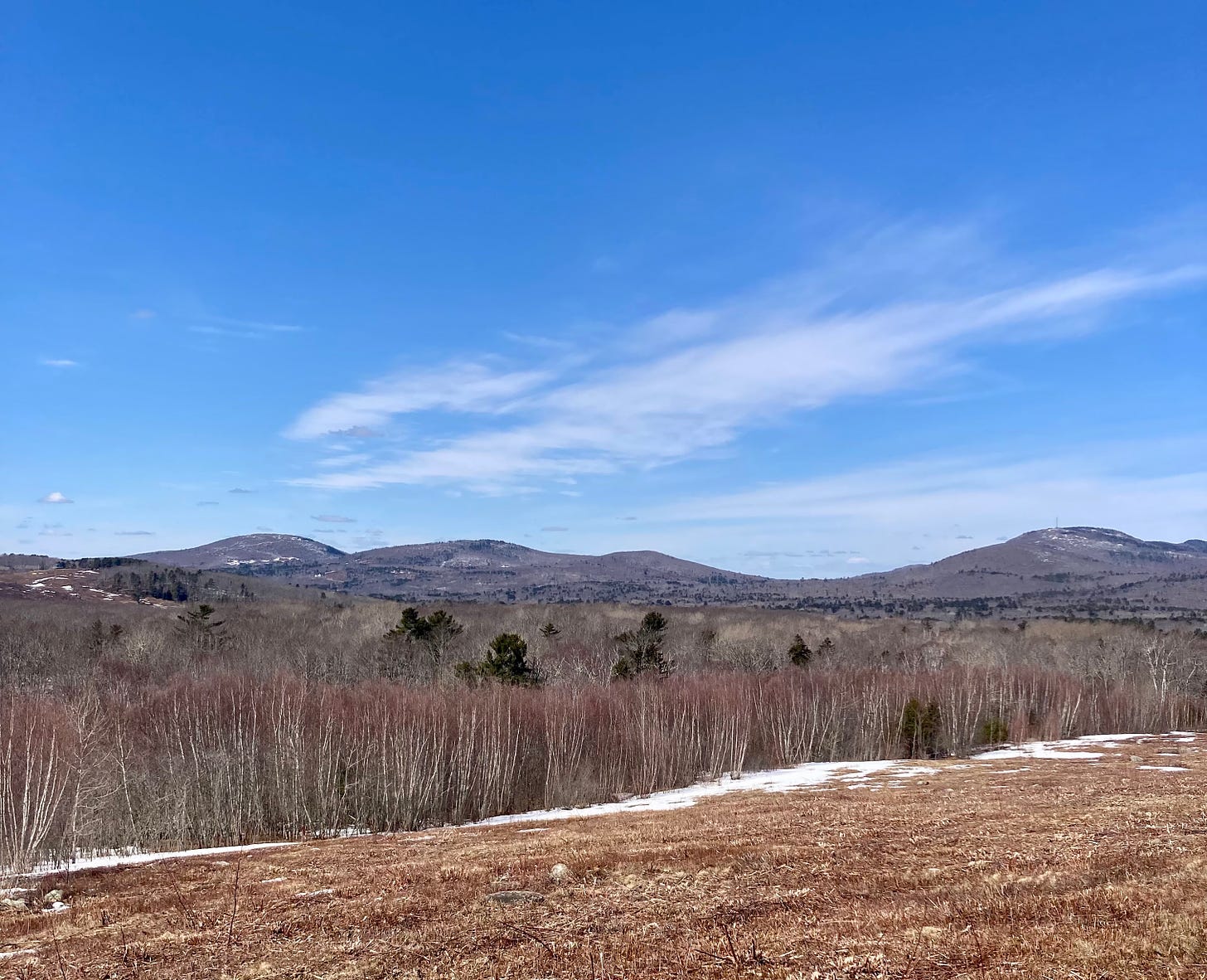 A view of hills and blue sky from a hike. Some snow remains visible, although most has melted.