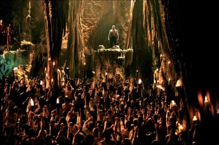 Morpheus (Lawerence Fishbourne) stands in front of a massive, diverse crowd of people in a cave co
