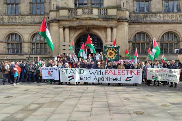 People standing outside Sheffield Town Hall. Many are holding red, black, white and green flags of Palestine. There are banners too, one of which says Stand with Palestine End Apartheid.