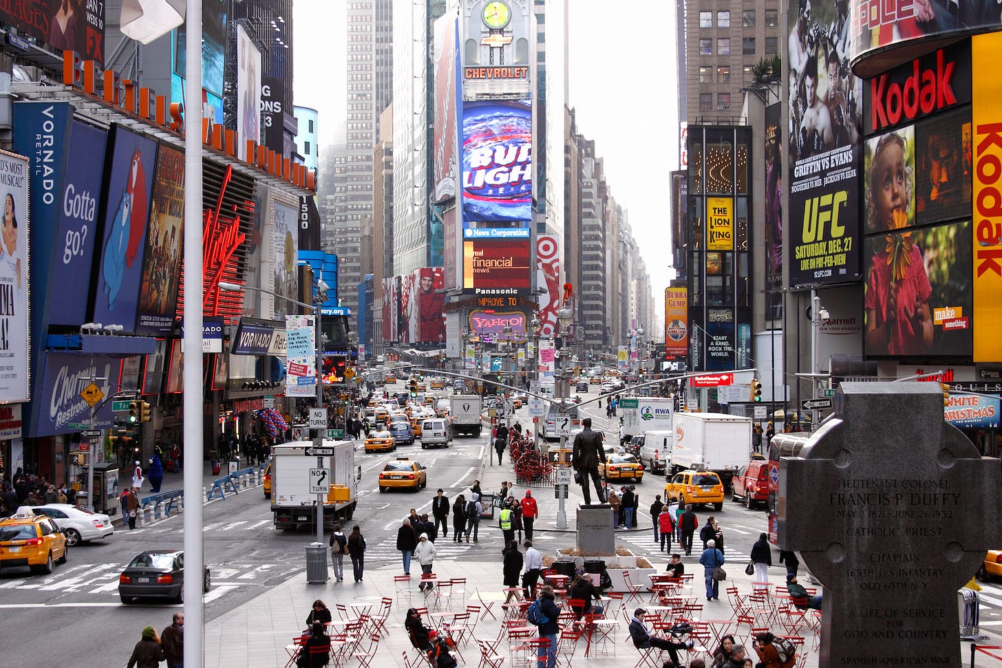 Street scene of Times Square in NYC, USA showing skyscrapers covered with ad billboards and flashing signs. Vehicles and pedestrians clog the streets below.   