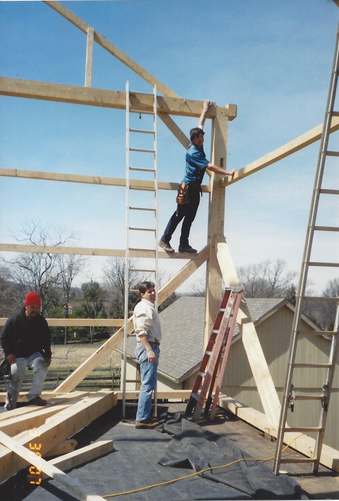 Workers stand on beams and near ladders as they begin framing a barn
