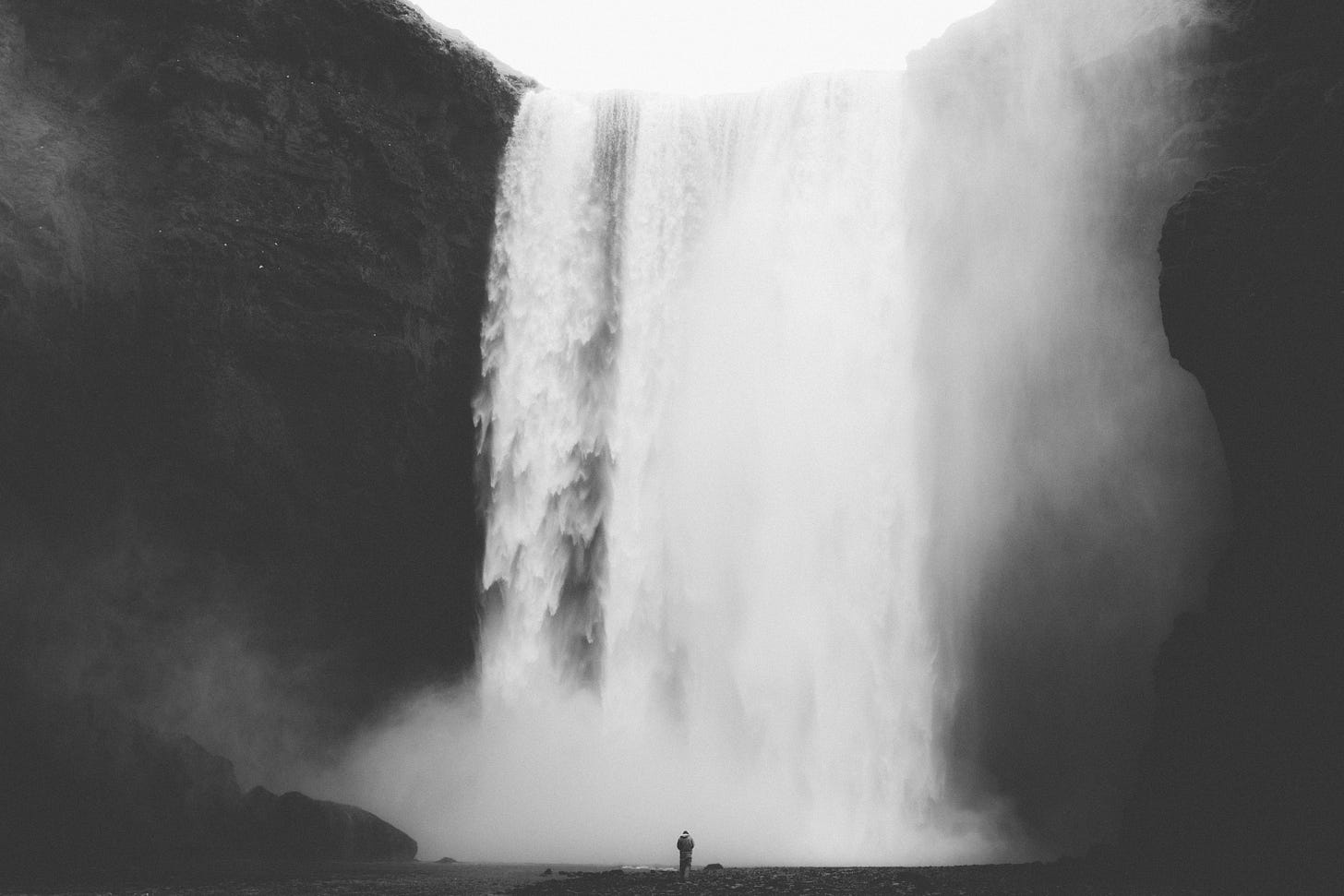 un'alta cascata tra rocce nere e una persona al suo cospetto