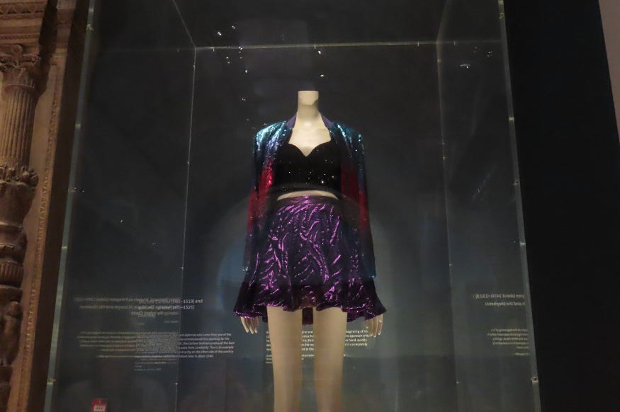 A mannequin wearing a purple sequin skirt, black sequin crop top and red and blue sequin jacket